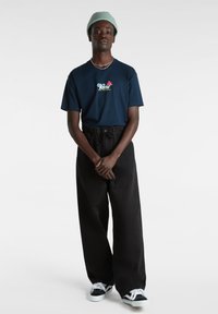 Granatowa bawełniana koszulka z haftowanym logo "Vans Off the Wall". Czarne spodnie o szerokich nogawkach, biało-czarne trampki oraz jasnoszara czapka beanie.