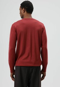 Bordeauxrode trui met lange mouwen, een geribbelde ronde hals, een gladde textuur en een getailleerde pasvorm, gecombineerd met broek met krijtstreepjes.