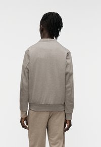 Γκρι φούτερ με ριμπ γιακά και μανσέτες, κατασκευασμένο από μαλακό ύφασμα, με ίσια γραμμή και μίνιμαλ σχεδιασμό, εμφανίζεται από πίσω.