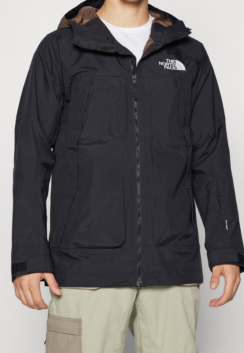 Chaqueta negra impermeable con capucha, que cuenta con un zipper frontal, dos grandes bolsillos y detalles de logotipo, fabricada con material suave y ligero.