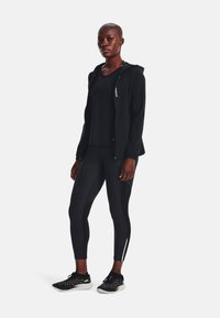 Čierny športový outfit pozostávajúci z mikiny na zips, topu s krátkym rukávom a legín s potlačou. Kontrastná textúra obuvi pridáva detail.