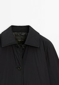 Manteau noir à manches longues avec col large, fermeture à boutons et doublure intérieure matelassée au niveau du col.