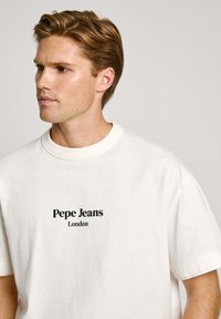 Bela bomba iz bombažne tkanine s črnim napisom "Pepe Jeans London" na sprednji strani. Oblika z okroglim ovratnikom, kratkimi rokavi in sproščenim fitom.