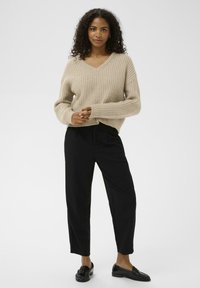 Beige knit sweater with a V-neck, long sleeves, and ribbed texture, paired with black tapered trousers and loafers.