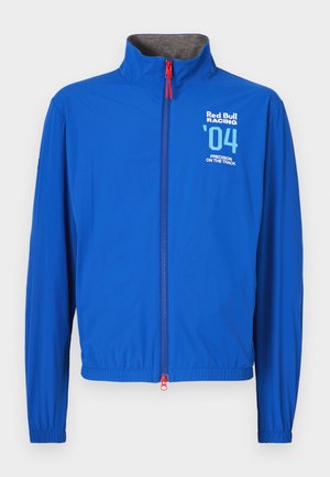 Modra lahka bunda z visokim ovratnikom, zadrgo po celotni dolžini in elastičnimi manšetami. Na njej so bele grafike: "Red Bull Racing," številka '04' in besedilo. Rdeč poteg zadrge.