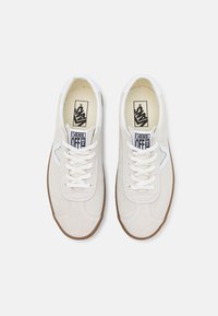 Baskets en suède beige clair avec des lacets blancs, une semelle en caoutchouc texturée et un petit accent bleu près du talon. Marquage sur la languette.