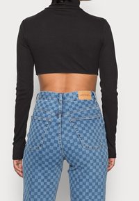 Svart ribbad polokragecropp topp ihop med blå rutiga högmidjade jeans. Anmärkningsvärda egenskaper inkluderar en beige etikett på jeansen.