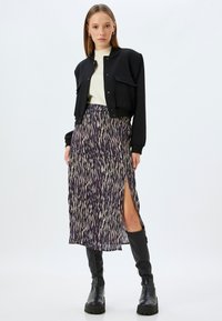 Veste bomber noir cropped avec fermeture à bouton, associée à une longue jupe à imprimé animal violet et une fente haute. Bottes noires montantes.