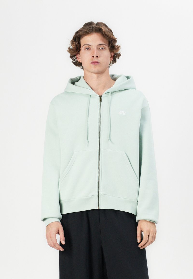 Light mint green zip-up hoodie made of soft fabric, featuring a kangaroo pocket and a logo on the left chest, with a relaxed fit.