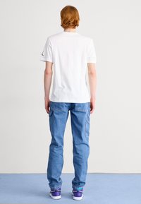Camiseta de algodón blanco con mangas cortas y cuello redondo; combinada con pantalones de mezclilla azul claro con bolsillos laterales y un corte relajado.