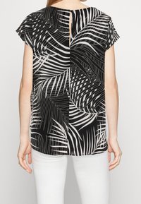 Top corto de manga corta en blanco y negro con un diseño de hojas, espalda dividida con cierre de botón y textura de tela suave. Llevado con pantalones blancos.