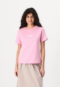 Lyserød bomuld T-shirt med rund hals og korte ærmer, prydet med et hvidt logo trykt på brystet. Kombineret med en beige nederdel.