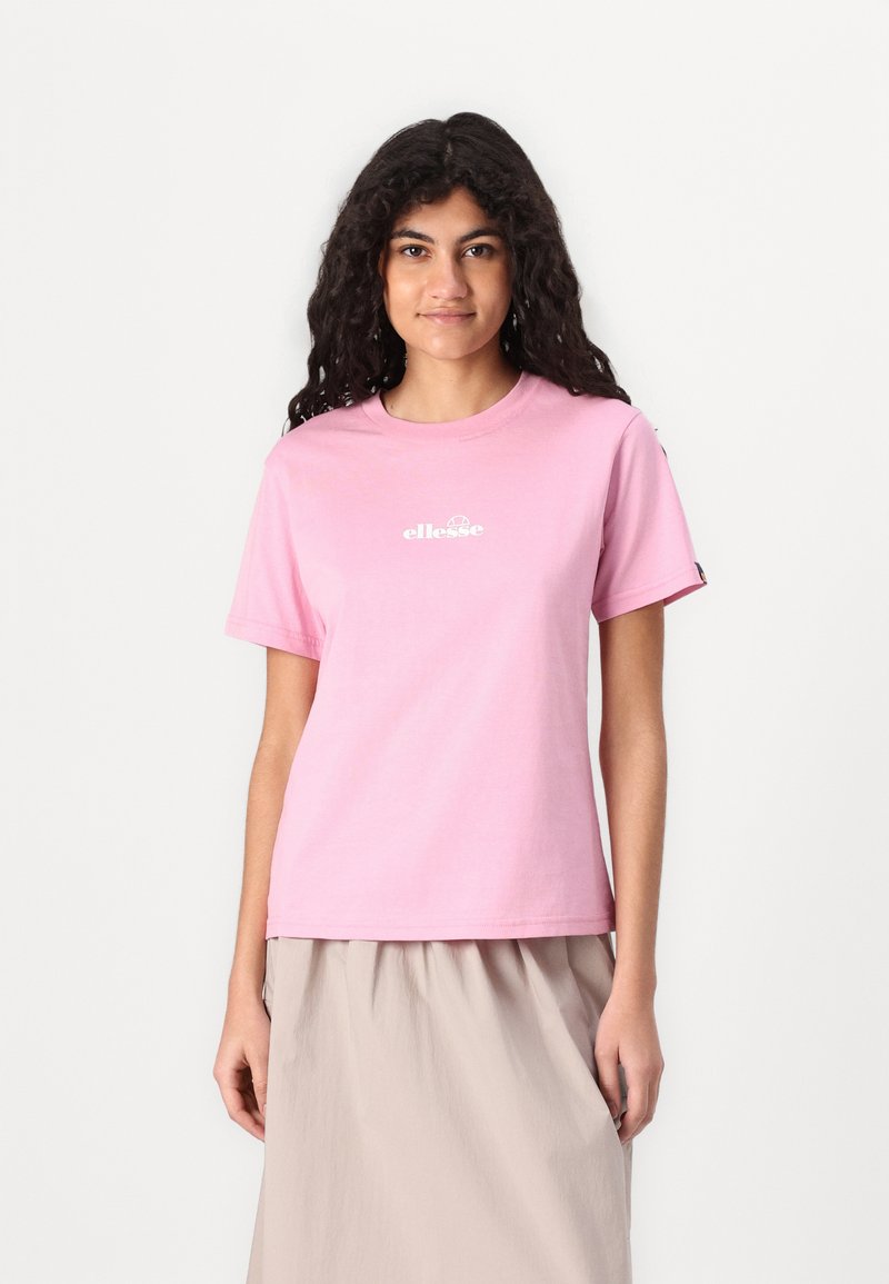 Lyserød bomuld T-shirt med rund hals og korte ærmer, prydet med et hvidt logo trykt på brystet. Kombineret med en beige nederdel.