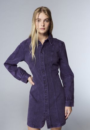 Vestito camicia in denim viola con maniche lunghe, chiusura a bottoni frontale e tasche laterali. Presenta una vestibilità strutturata e dettagli di cucitura visibili.