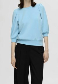 Jersey de color azul claro con mangas abullonadas, escote redondo y puños elásticos, combinado con pantalones negros de corte ajustado. Textura de tela suave.