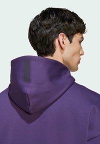 Felpa con cappuccio viola dal tessuto morbido. Presenta un'etichetta nera minimalista sul retro del cappuccio che mostra un design pulito.