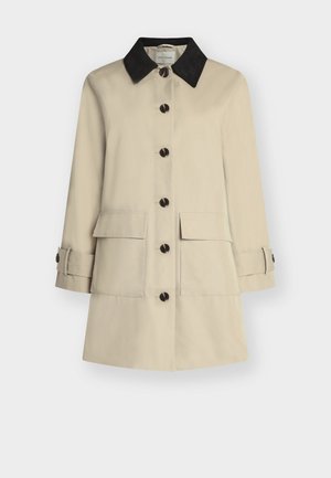Beige knelang kåpe med mørkr fôr, knapper foran, to klafflommer foran og knappede stropper på lange ermer.