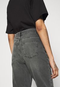 Jeans de mezclilla gris de cintura alta con corte recto, que cuentan con dos bolsillos traseros y un acabado de tela texturizada.