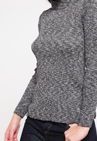 Grau gestrickter Rollkragenpullover mit einer strukturierten Strickmuster, langen Ärmeln und einer taillierten Passform, kombiniert mit dunkelblauen Jeans.