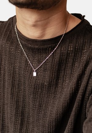 Silver chain necklace featuring a rectangular pendant, worn over a textured black sweater with vertical ribbing.