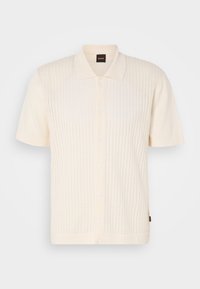 Polo à manches courtes, de couleur crème, avec une texture à côtes verticales, fermeture à cinq boutons et un col classique. Fabriqué en tissu doux.