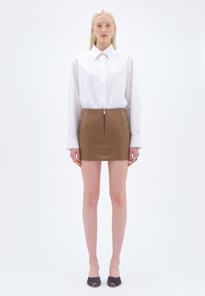 Camicia bianca con colletto, gonna mini in pelle marrone con zip frontale e décolleté grigi aperti. Tessuto liscio con una vestibilità strutturata.