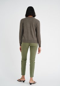 Maglione marrone lavorato a maglia con scollo rotondo, abbinato a pantaloni verdi slim-fit. Presenta maniche lunghe e tessuto testurizzato.