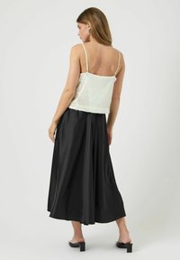 Biały crop top z cekinami na cienkich ramiączkach, w zestawieniu z długą czarną satynową spódnicą o zwiewnym kroju i gładkiej fakturze.