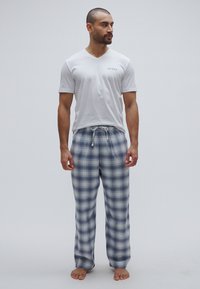 Tricou alb de bărbați din bumbac cu guler în V și logo "GUESS"; pantaloni de pijama în carouri, în tonuri de albastru și gri, cu talie elastică și șnur reglabil.