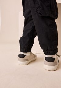 Hõbedased tennised mustade detailidega, ülaosa on seemisnahast ja nahast. Püksid mustast kangast, kummiga sääreotsad. Valged sokid on nähtaval.