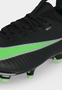 Μαύρο ποδοσφαιρικό παπούτσι Nike με πράσινο λογότυπο, μαύρα κορδόνια και πράσινες ακμές στα ήλεκτρα σε λευκό φόντο.