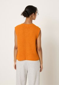 Oranje mouwloos gebreid topje met een textuurafwerking, met een ronde halslijn en een losse pasvorm, gecombineerd met lichtgrijze broek.