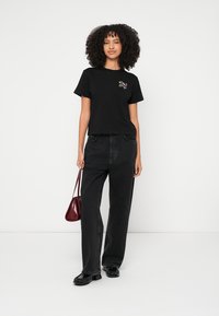 Camiseta negra de algodón con mangas cortas, con un detalle de bordado floral. Combinada con vaqueros negros de talle alto y un pequeño bolso burdeos.