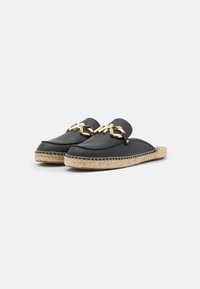 Scarpe slip-on in pelle nera con un accentuato decorativo dorato e suola in juta stile espadrillas. Punta rotonda e design piatto e flessibile.