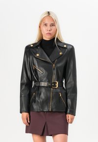 Black leather jacket with gold hardware, zippered pockets, and a belted waist. Features a classic lapel and smooth texture.