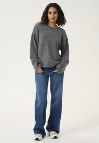 Grey knit sweater with loose sleeves, paired with light blue flared jeans. The model wears white sneakers and stands on a plain background.