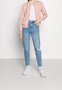 Lichtroze gewatteerd bomberjack over een wit t-shirt, gecombineerd met lichtblauwe high-waisted gescheurde jeans en witte sneakers.