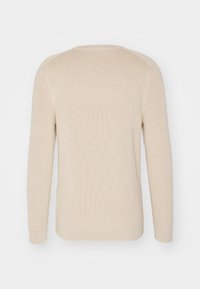 Beige ribbad stickad tröja med långa ärmar, rundad hals och texturerat tyg. Har en något avsmalnande fåll och sömlös axeldesign.