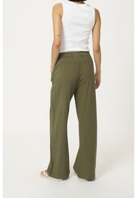 Pantalons verts à jambes larges avec un tissu texturé et une taille élastique, assortis à un top sans manches blanc, vus de dos.