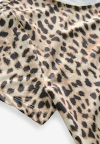 Leoparda raksts audums izceļas ar brūnganu fonu, uz kura ir tumši brūni un melni punkti, gluda tekstūra un maiga apdare. Redzama daļēja piedurkne.