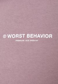 Lila textil med vittryckt text: "© VÄRSTA BETEENDE PREMIUM 120Z 340Gr/m²." Slät textur med ett medeltungt tyg.