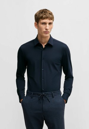 Navy long-sleeve shirt made of textured fabric, featuring a classic collar and button-down front. Paired with patterned dark trousers.