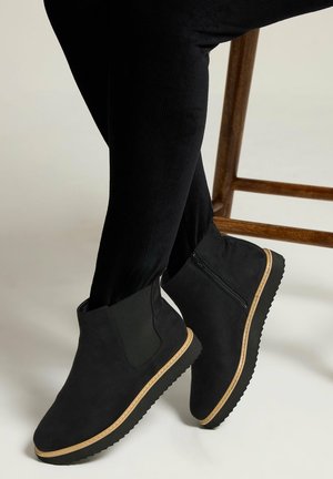 Czarne zamszowe botki za kostkę z elastycznymi panelami i zapięciem na zamek, z teksturowaną gumową podeszwą z kontrastowym jasnobrązowym wykończeniem.