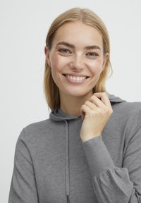 Grau Kapuzenpullover mit geripptem Bund und Kordelzug. Der Stoff wirkt weich und leicht strukturiert, mit einer lässigen Passform.