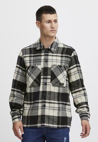 Svart-hvitt rutete flanellskjorte med to frontlommer, knappelukking og krage. Stoffet ser teksturert og varmt ut.