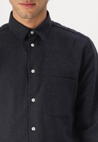 Cămașă button-up de un albastru închis realizată dintr-un material texturat, având guler, placket frontal cu butoane și un singur buzunar pe piept.