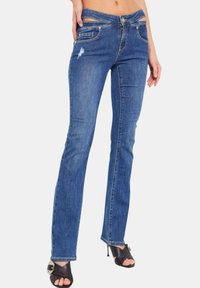 Jeans in denim blu con una vestibilità slim, caratterizzati da un design con ritaglio in vita, dettagli strappati, cinque tasche e chiusura con zip.
