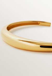 Brazalete de metal en tono dorado con una superficie lisa y pulida, que presenta un diseño elegante y redondeado, con bordes sin costuras. Sin patrones ni acentos visibles.