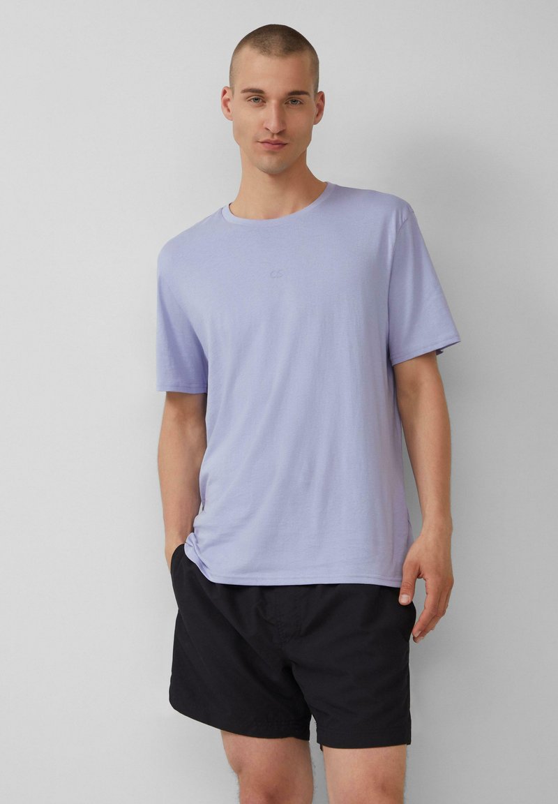 Lila kortekorte t-shirt met een ronde hals, gemaakt van zachte stof, gecombineerd met zwarte korte broeken. Beschikt over een klein logo op de borst.