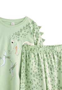 Ensemble de pyjama sur le thème des dinosaures verts, comprenant un haut à manches courtes et un pantalon avec taille élastique. Le haut comporte des pics et des graphiques de dinosaures amusants.